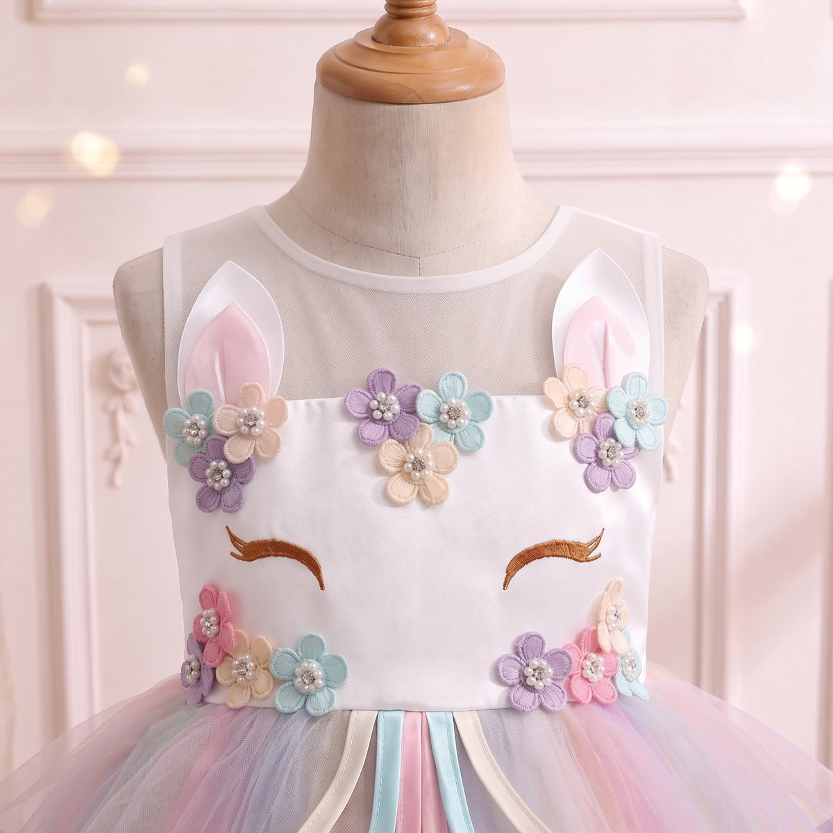 Close up of the white unicorn-face bodice: standing ears, pearl-centered pastel flowers and golden embroidered lashes