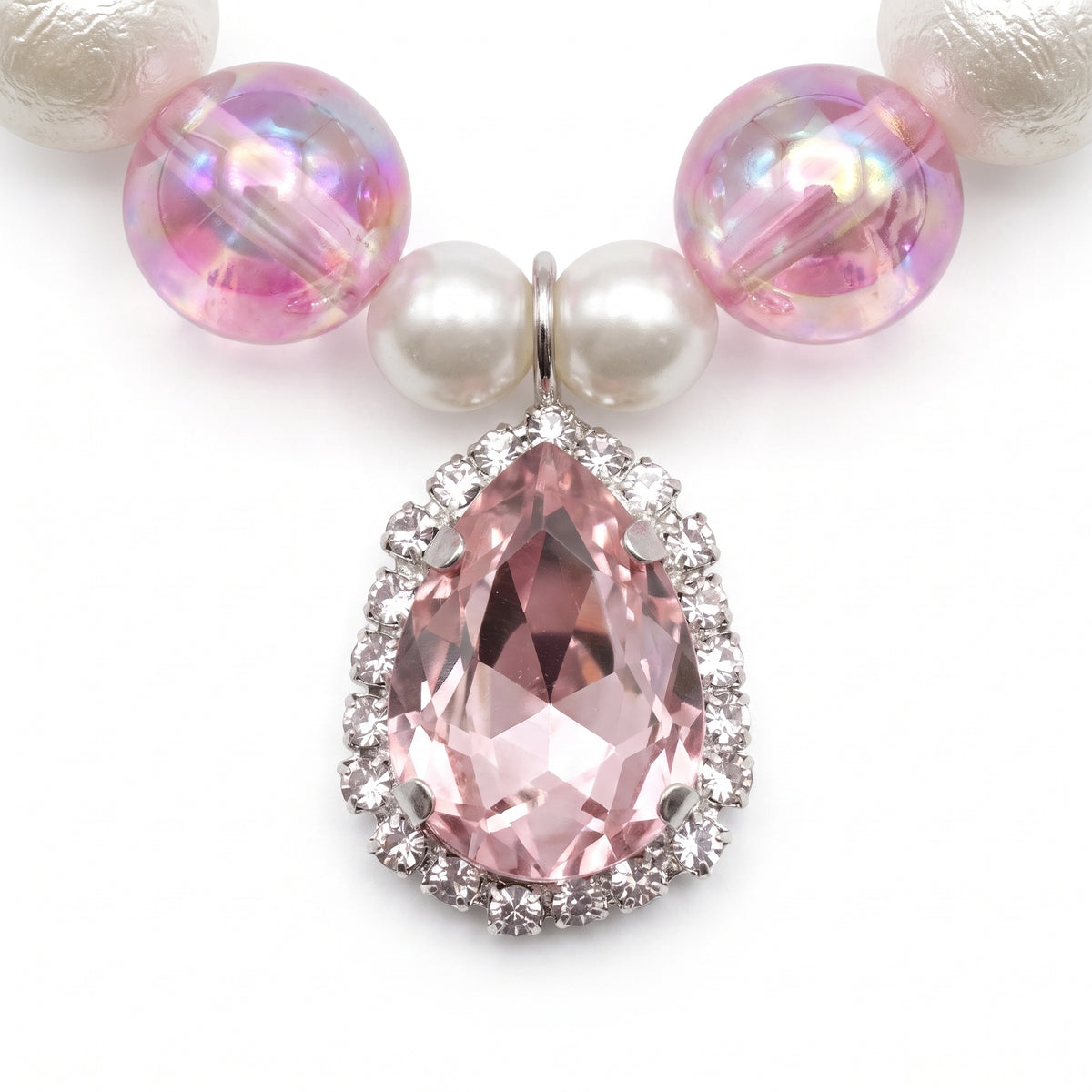 Close up of the pink teardrop pendant edged in rhinestones between pearl and iridescent pink beads