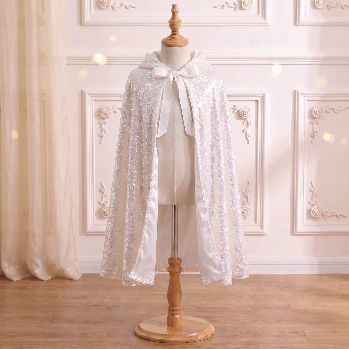 Front view of the Ice Queen Frostlight Cape on a mannequin: iridescent sequins and white ribbon ties