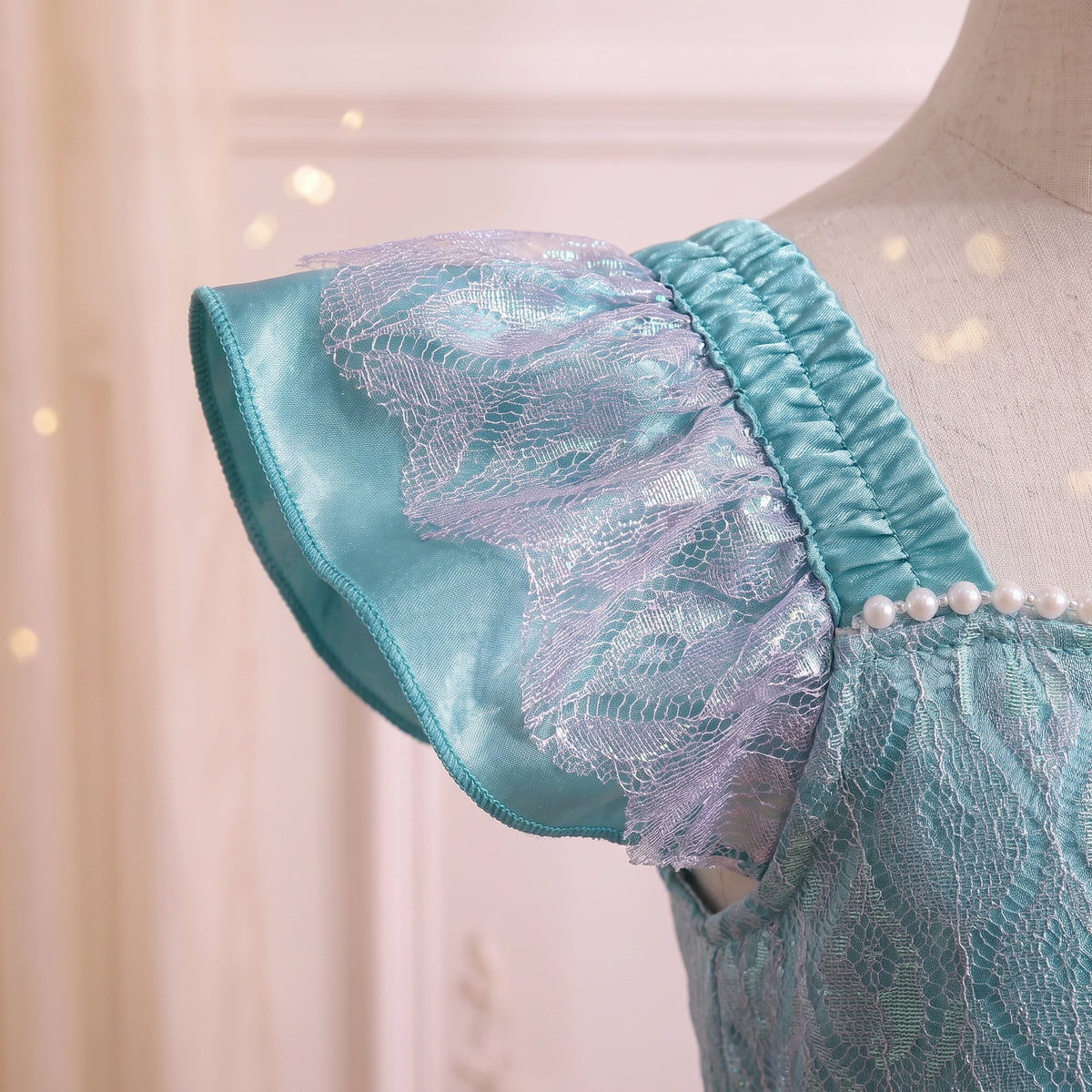 Close up of a lace-trimmed aqua flutter sleeve with pearl edging