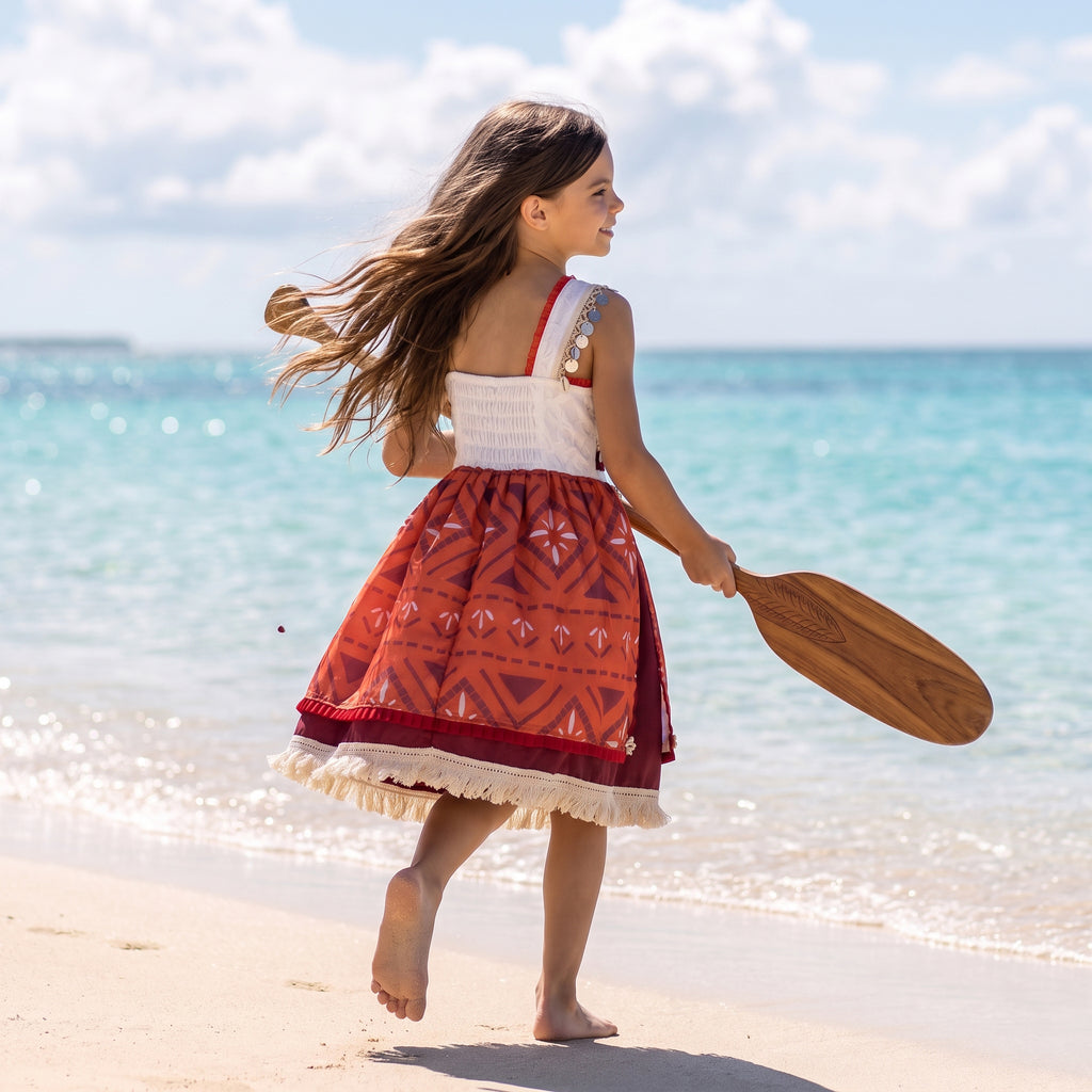 Back view of the island princess dress showing the smocked stretch panel and twirling tapa print skirt on the beach