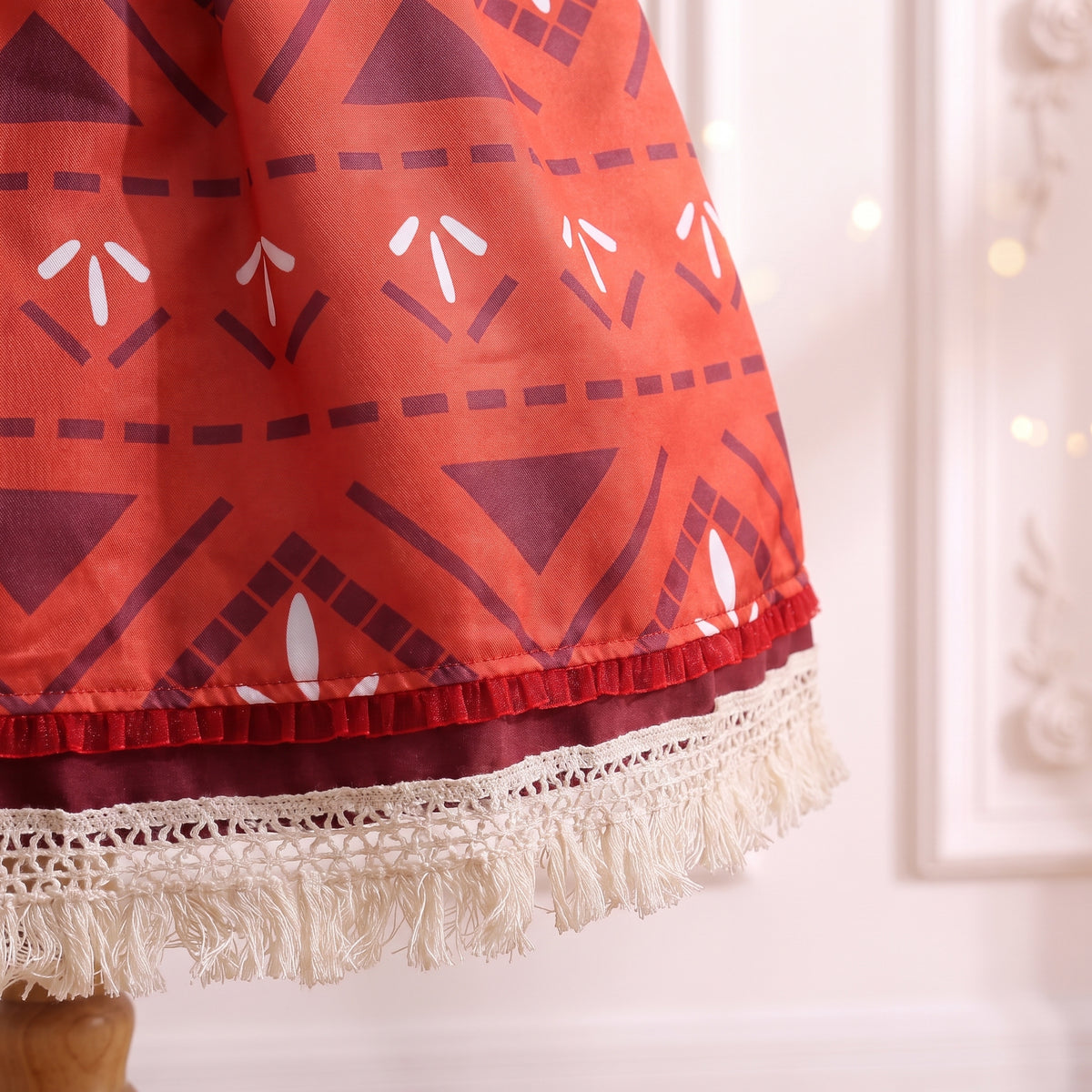 Close up of the hem with pleated crimson ribbon and cream crochet fringe